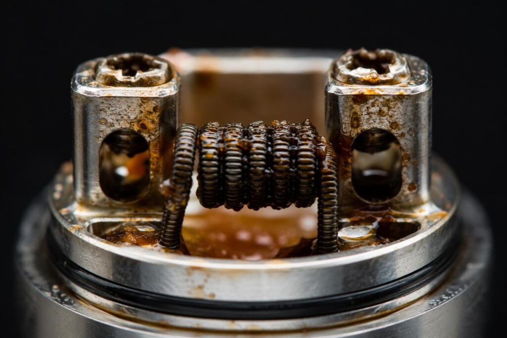 Macro-level visualization of coil residue accumulation caused by sucralose and complex flavor compound caramelization during vaporization — illustrating the primary mechanism by which sweet, complex e-liquids reduce coil lifespan in B2B e-liquid formulation contexts.